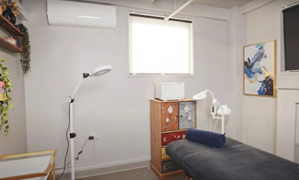 Compact beauty treatment room for rent in Manhattan with therapy bed and professional magnifying lamp.