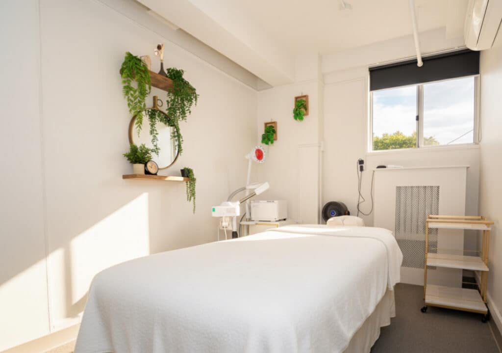 Bright treatment room for rent in NYC with massage bed, white linens, and greenery decor for beauty and acupuncture.