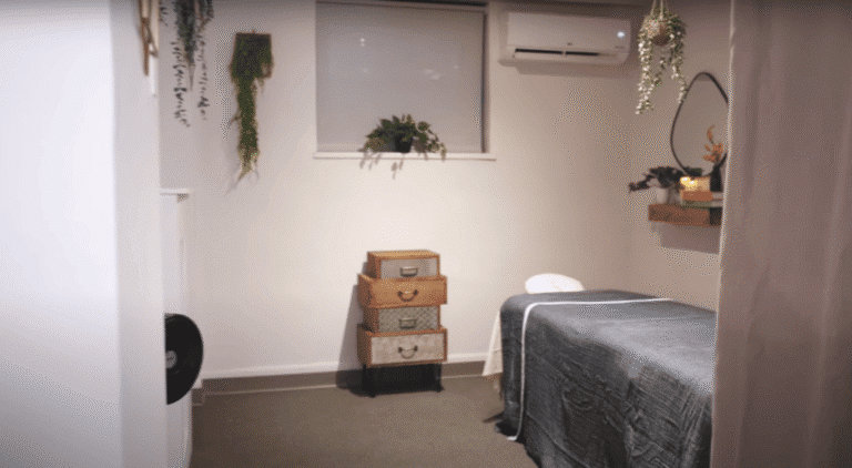 Modern massage treatment room for rent in NYC with cozy lighting, plants, and wooden shelves.