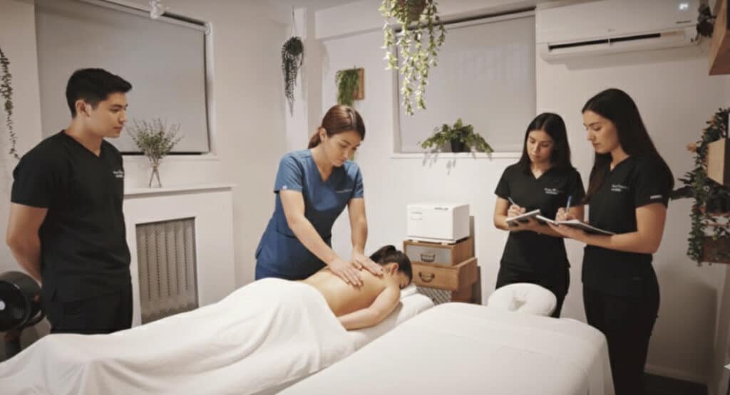 Massage instructor demonstrates technique to students during hands-on class in NYC treatment training room.